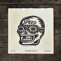 Black and white skull design with 'SPEED' text on a textured paper against a wooden background