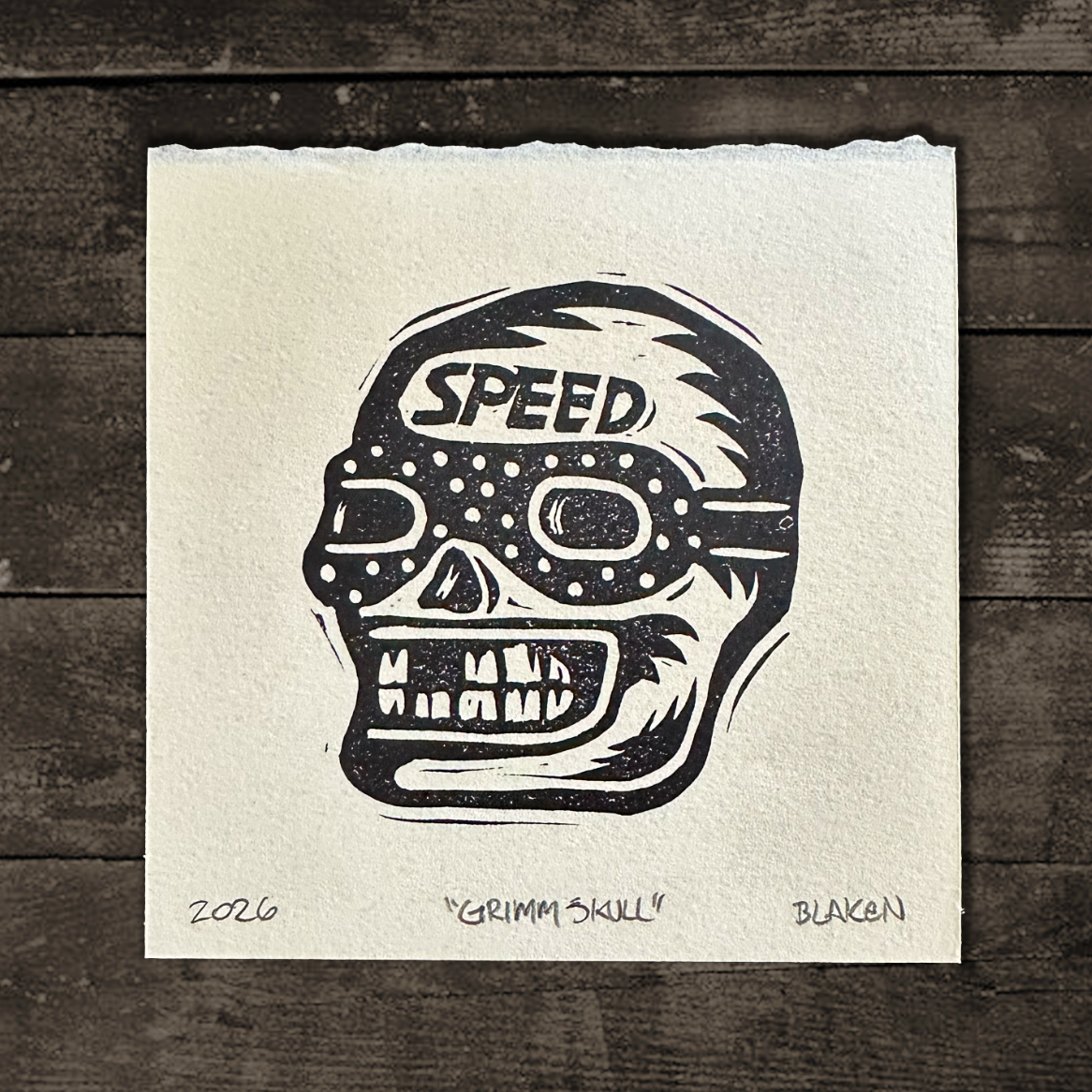 Black and white skull design with 'SPEED' text on a textured paper against a wooden background